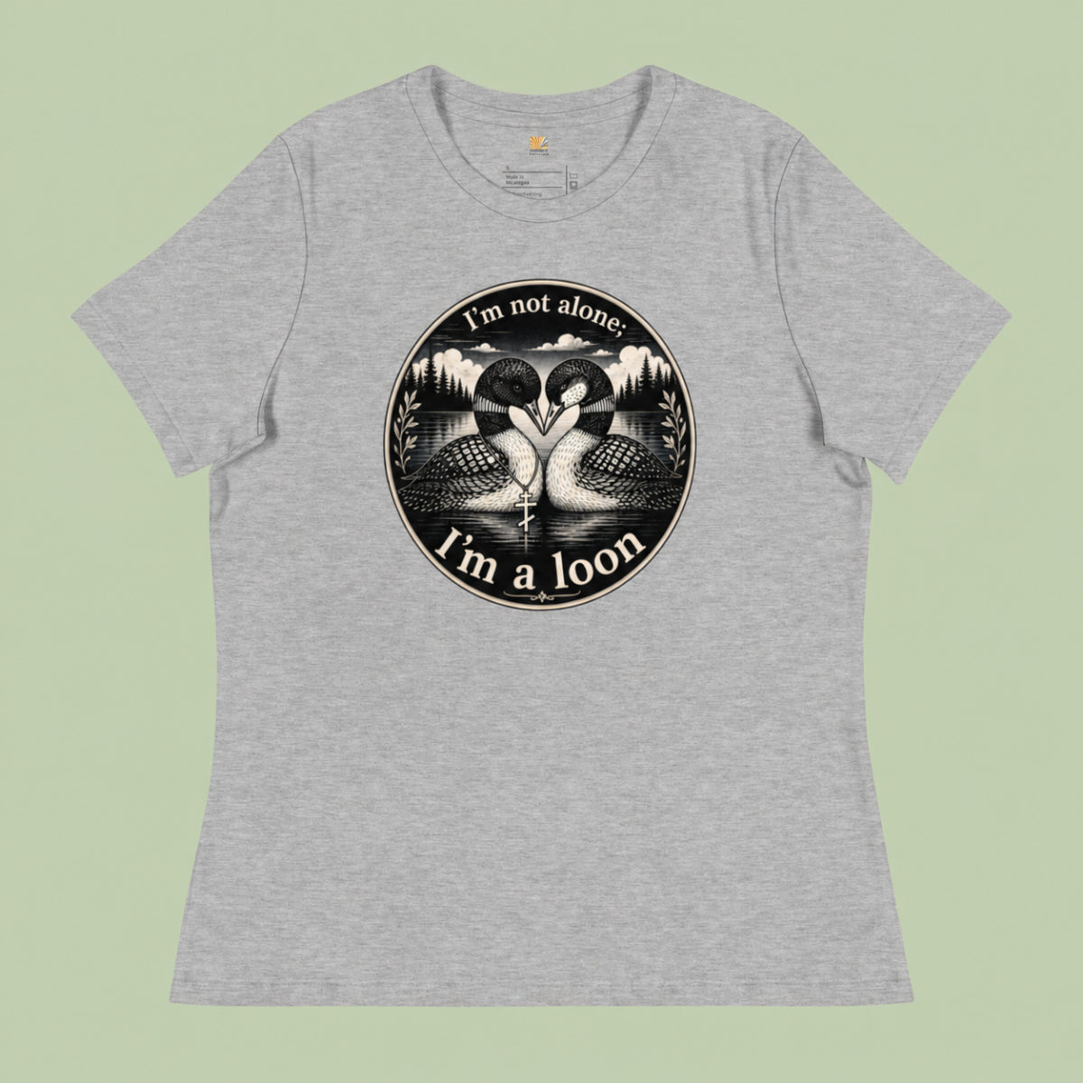 A heather gray short-sleeve crewneck t-shirt featuring a circular black and white graphic of two swans facing each other in a lake, with the text 'I'm not alone. I'm a loon' printed around the design.