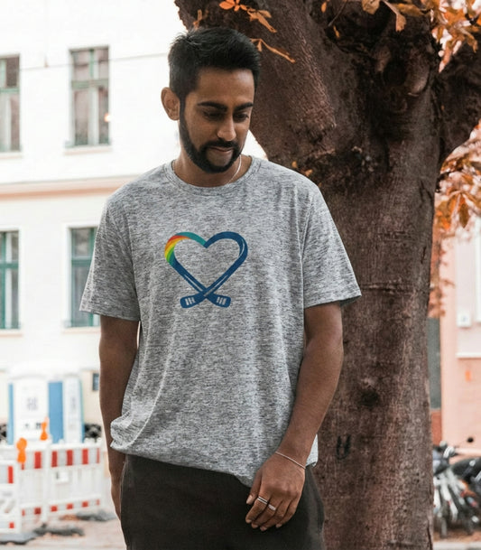 Man wearing a gray t-shirt with a hockey stick heart and rainbow design, standing outdoors.
