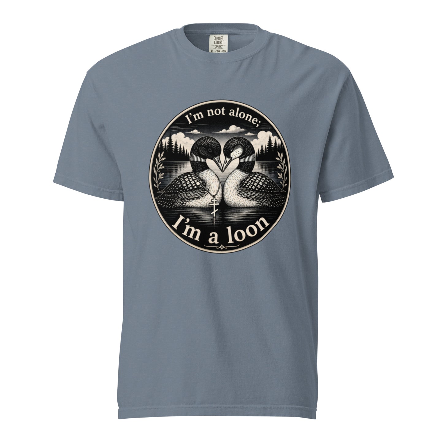A Blue Jean colored short-sleeve crewneck t-shirt featuring a circular black and white graphic of two loons facing each other in front of a lake and mountains, with the text 'I'm not alone. I'm a loon'.