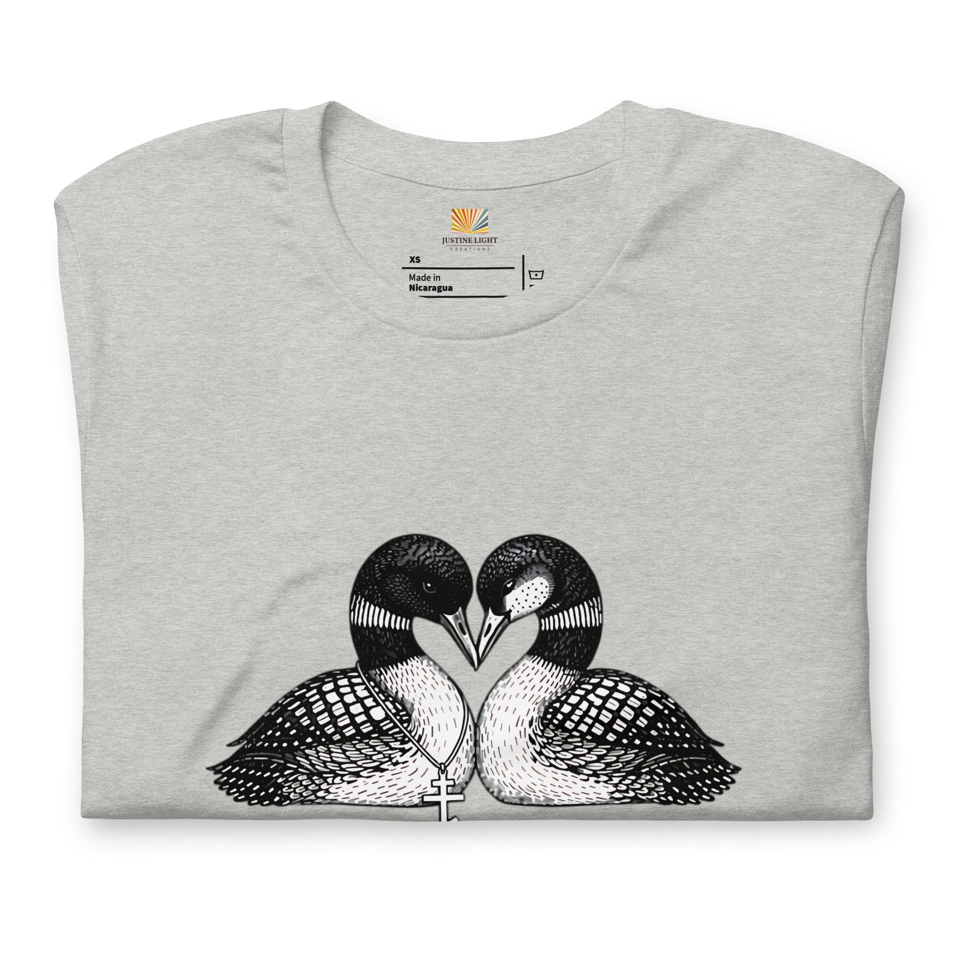 Folded image of hockey romance loon t-shirt with a graphic of two birds, with beaks together forming a heart. Athletic Heather color shirt