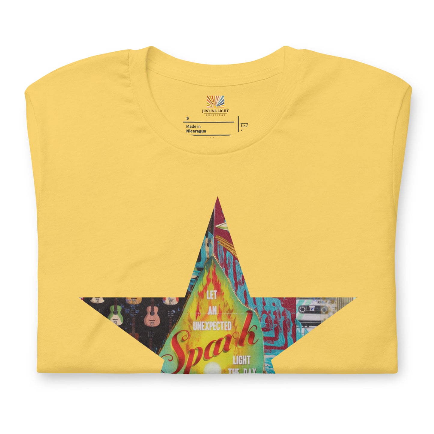 A folded yellow Star tee shirt with a colorful mixed-media star design and the words spark of inspiration on a soft unisex t shirt.
